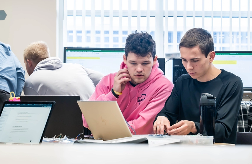 Students working on computer and electronics projects in a classroom lab.